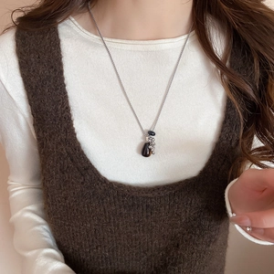 Detail of silver tassel necklace with dark teardrop pendant worn on white knit sweater