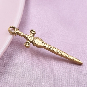 Macro shot of gold sword pendant in 304 stainless steel on soft pink fabric