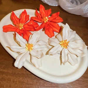 Close-up of oversized acrylic flower earrings in orange and white on a ceramic plate