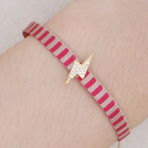 Close-up of pink striped woven bracelet featuring a gold lightning bolt charm with crystals
