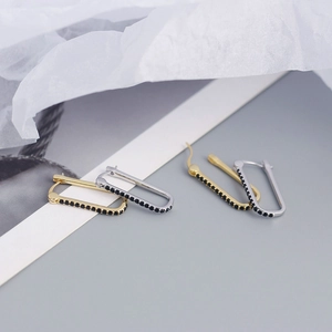 Detail of silver and gold geometric earrings with inset black stones on grey background
