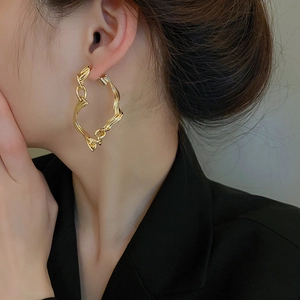 Close-up of golden irregular twisted hoop earrings with chain link details on a model