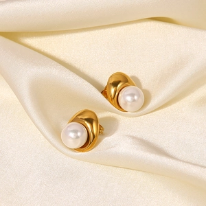Detail of elegant gold geometric pearl earrings on beige silk fabric background