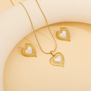Golden heart necklace and earrings set with white pearl inlay on warm beige background