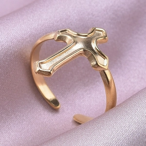 Detail view of a gold cross adjustable ring on elegant purple silk fabric background