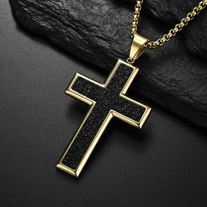 Detail of matte black cross pendant with gold edges on dark rock background