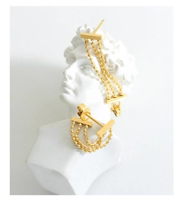 Détail de boucles d'oreilles pompon à trois couches de chaînes dorées sur sculpture