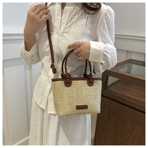 Close-up of straw woven handbag with dark brown leather handles and adjustable strap