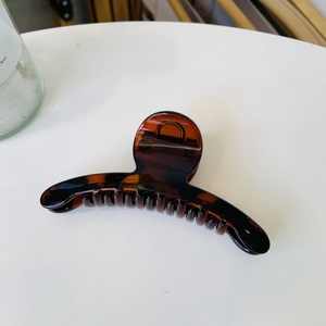 Close-up of amber brown resin hair claw clip with a sleek curved design on a white surface