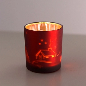Detail of red glass reindeer candle holder with etched snowy cabin and golden interior glow