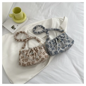 Close-up of textured pleated fabric with floral chain detail on beige and blue underarm bags