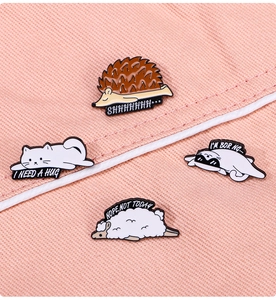 Cute animal enamel pins featuring sleepy cat, hedgehog, and sheep on pink fabric