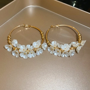 Detail view of gold hoop earrings with white acrylic flowers on a golden display tray