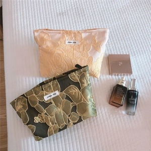 Detail of floral embossed embroidery cosmetic bags in champagne and dark green silk