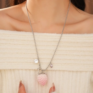 Close-up of strawberry pendant necklace with heart gemstone and star on a white sweater