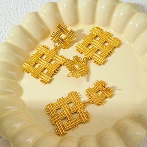 Retro geometric woven gold titanium steel earrings displayed on a white ceramic plate