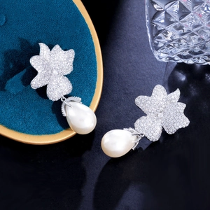 Macro shot of silver petal-shaped zircon earrings with elegant drop pearl details