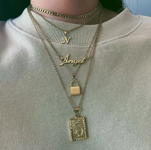 Detail of layered gold necklaces with letter N, Angel pendants and dragon embossed charm