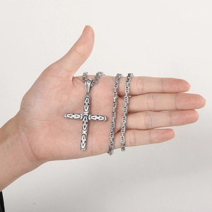 Close-up of a silver cross pendant with a thick Byzantine chain held in hand