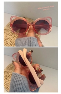 Pink translucent glitter cat-ear children's sunglasses with gray lenses in hand