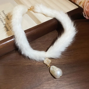 Detailed close-up of a plush choker featuring a gold clover pendant and a baroque pearl