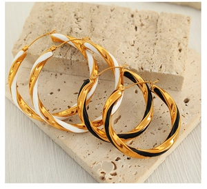 Detailed shot of large twisted hoop earrings in gold with black and white drip oil finish