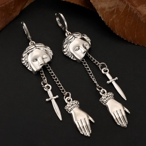 Detailed view of silver gothic earrings with mask, sword and hand charms on black background