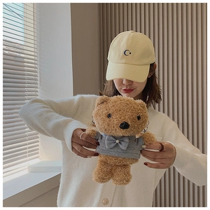 Detail of cute brown plush bear crossbody bag held by a model in casual grey clothing
