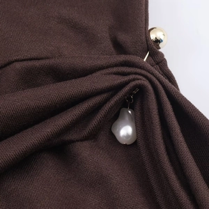 Detailed close-up of dark brown knit fabric with gold beads and pearl drop charm pins