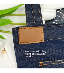 Dettaglio della borsa tote in denim blu scuro con patch in pelle e cuciture a contrasto