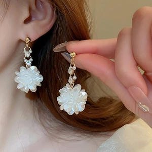 Dettaglio orecchini a fiore con petali bianchi, catena dorata, perle e strass brillanti sulla pelle