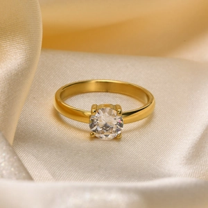 Close-up of a gold-plated titanium ring with a round clear zircon on champagne silk fabric