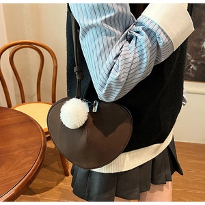 Detail der dunkelbraunen herzförmigen Umhängetasche mit weißem Plüschball und Matt-Finish