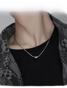 Close-up detail of silver snake bone chain with checkered square pendant on neck