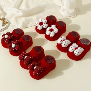 Red baby socks with knit texture, white polka dot flowers and bow accents on soft fabric