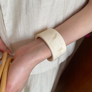 Detail of a wide cream resin bangle with subtle gold marble textures on a model's wrist