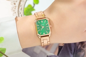 Close-up of rose gold rectangular watch with green dial and rhinestones on a wrist