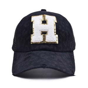 Detail of distressed mesh baseball cap featuring a sequined letter H patch and worn texture