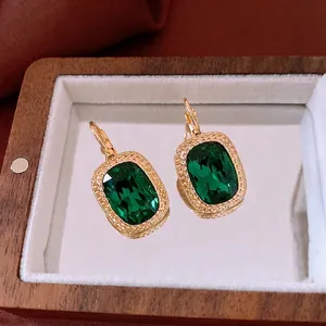 Vintage gold earrings with emerald green rectangular stones on luxury velvet background