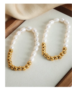 Detail of freshwater pearl and golden steel bead handmade bracelet on a soft grey display