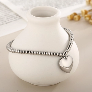 Detailed view of silver beaded bracelet with heart pendant on white ceramic vase