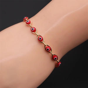 Detailed shot of gold-plated red Evil Eye bracelet on wrist against dark background