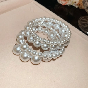 Macro view of multi-layered white pearl bracelets on a beige matte display stand