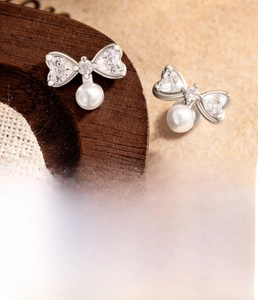 Detail of silver bow pendant earring with heart-shaped zircon and white imitation pearl