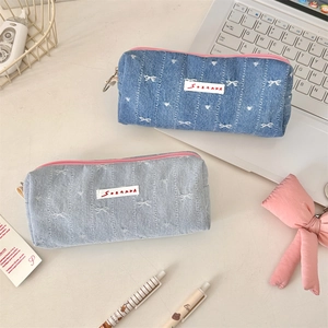 Close-up of denim pencil cases with bow embroidery and pink zipper on a desk