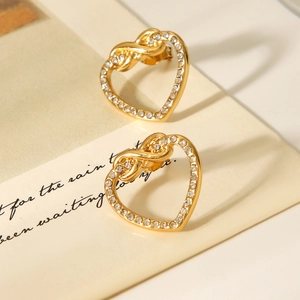 Close-up of heart-shaped gold earrings with knot design and sparkling zircon inlays