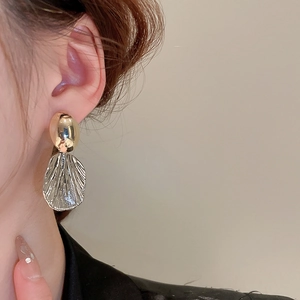 Close-up of a two-tone oval and fan-shaped metallic earring worn on a female model