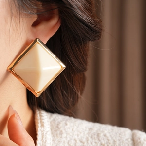 Close-up of geometric square stud earring with off-white resin and gold metallic edging