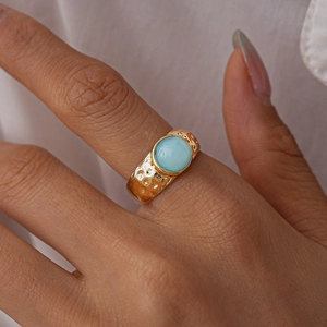 Gros plan d'une bague martelée dorée ornée d'une pierre précieuse ronde bleu clair