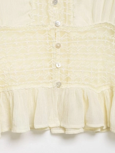 Detail view of beige lace blouse featuring ruffled edges and elegant pearl buttons